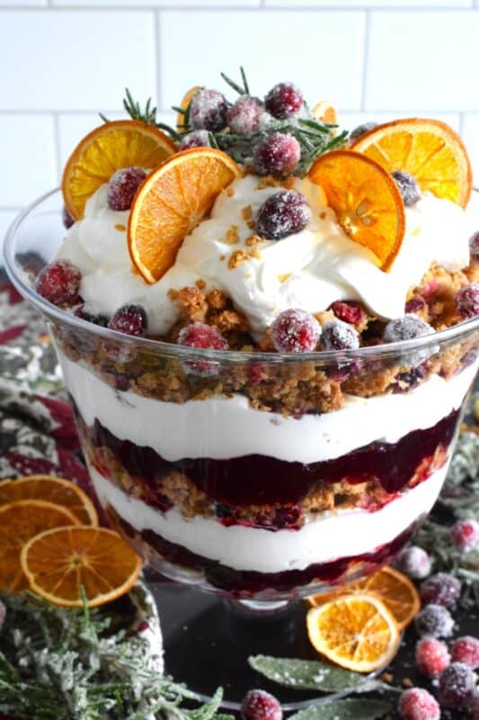 Freshly homemade cranberry squares are crumbled and layered with a delicious orange and rosemary-infused whipped cream. Topped with sugared cranberries and rosemary, this Orange Cranberry Trifle is a mouthwatering, showstopping holiday dessert! #trifle #cranberry #orange